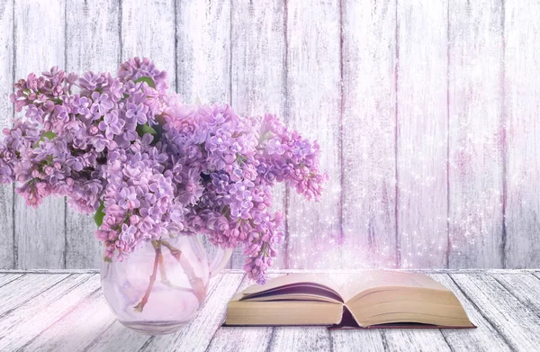 Intérieur de la chambre avec des fleurs lilas dans un vase en verre et livre ouvert — Photo