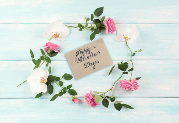 Top view of floral frame consists of roses and orchids flowers and greeting card for Valentine's Day on wooden background in shabby chic style