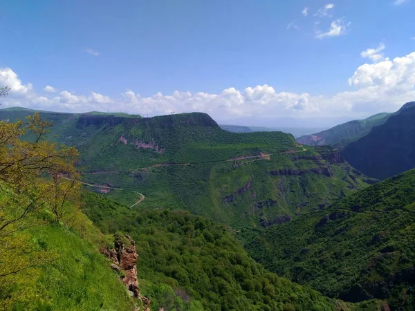 Caucasus Mountains of Armenia, a deep canyon Harsnadzor covered with green vegetation, along the edge of which there is a road. against a blue sky with clouds