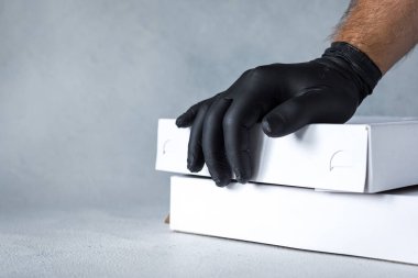 Ev teslimatı, online sipariş. Kutulu lastik eldivenler, ellerinde bir paket. Karantina sırasında yiyecek ve market teslimatı