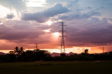 Günbatımı saatinde yüksek voltajlı elektrik kulesi ve günbatımı arka planında kavis olan gökyüzü.