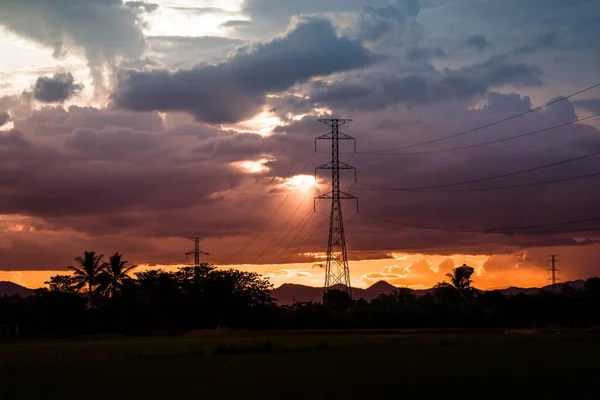 日没時の高電圧電気塔と日没の背景に雲と空 — ストック写真