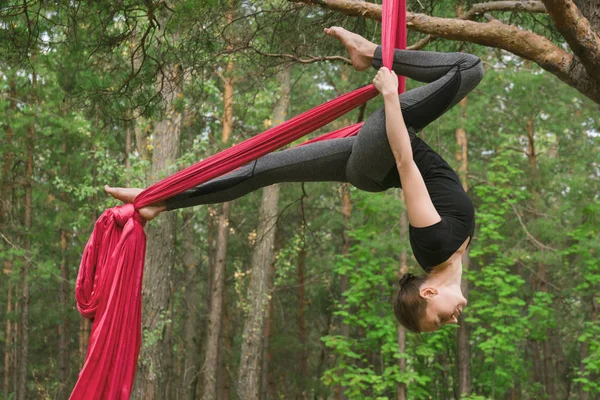 Young woman practicing aerial yoga exercise or antigravity yoga outdoors. Flying, fitness, stretch, balance, healthy lifestyle people. Woman using hammock.