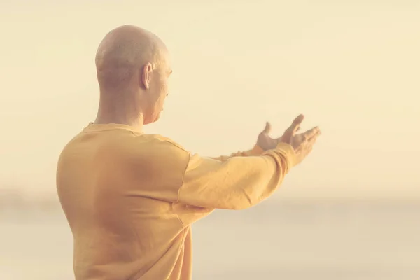 Young athletic man rising hands on sunset sky. Meditation, yoga, freedom and healthy lifestyle concept