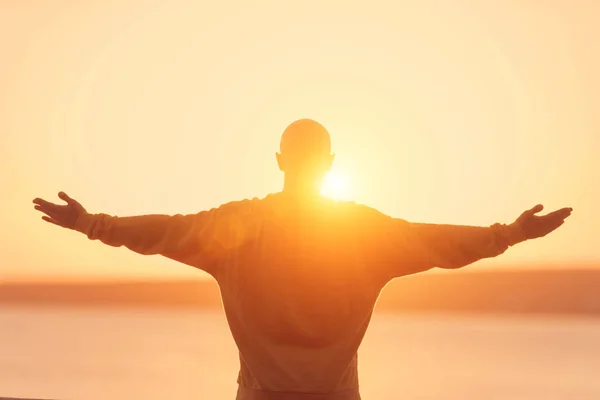 Yükselen genç atletik erkek günbatımı gökyüzü üzerinde eller. Meditasyon, yoga, özgürlük ve sağlıklı yaşam konsepti