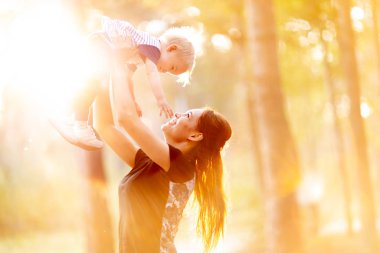 Genç Anne oğlunu tutar. Kadın bir yaz parkta küçük bebeği ile eğleniyor. Açık havada oynarken mutlu anne çocuk kadar atar