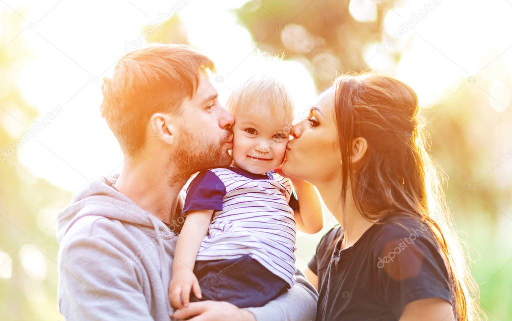 Young parents hugging and kissing her baby. Happy family outdoors. 