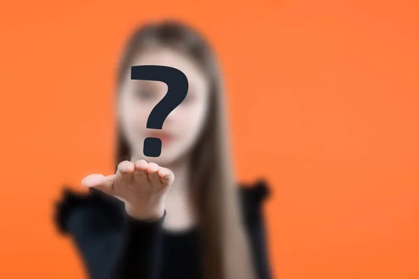 Child girl with blurred face holding question mark over orange background. Problem concept.