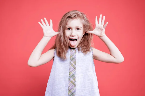一个有趣的小女孩的肖像显示舌头对相机在粉红色的背景 — 图库照片