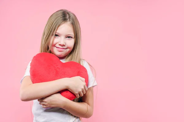 Portrait of cute little girl hugging red heart over pink background. Valentine\'s Day. Mothers Day.