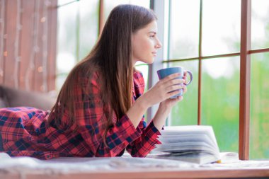 Bir fincan çay ve bir kitap ile pencereden dışarı bakarak hayalleri güzel bir genç kızın bir profil.