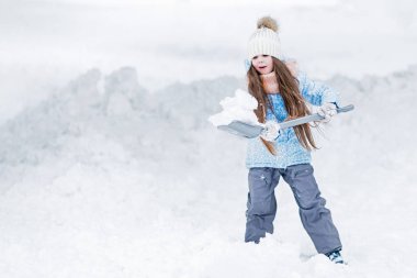 Uzun saçlı kız çocuk kar kürekle. Sağlıklı açık hava etkinlikleri ve yardımcı anne kavramı.