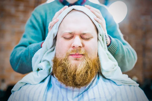 A closeup of man with red mustache and beard is being dried his head with a towel in barbershop.