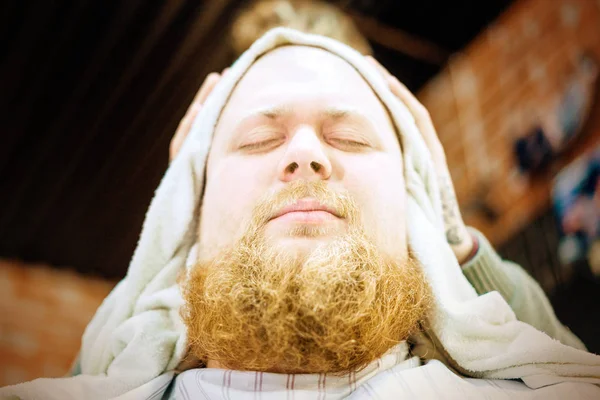 A closeup of red bearded man with towel on head. He screwed eyes up.