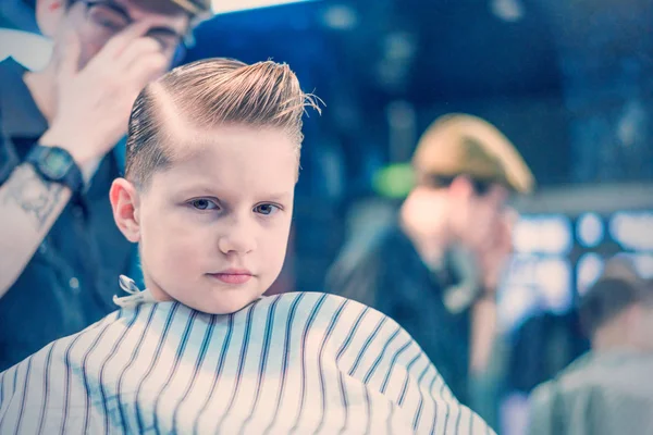 ファッショナブルな散髪理髪店で座っていると疲れて探してカメラを持つ少年 — ストック写真