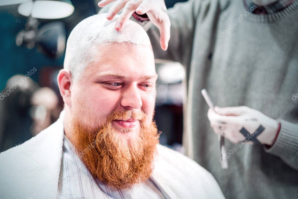 A barber's tool in hand for shaving head of a bald man with beard.