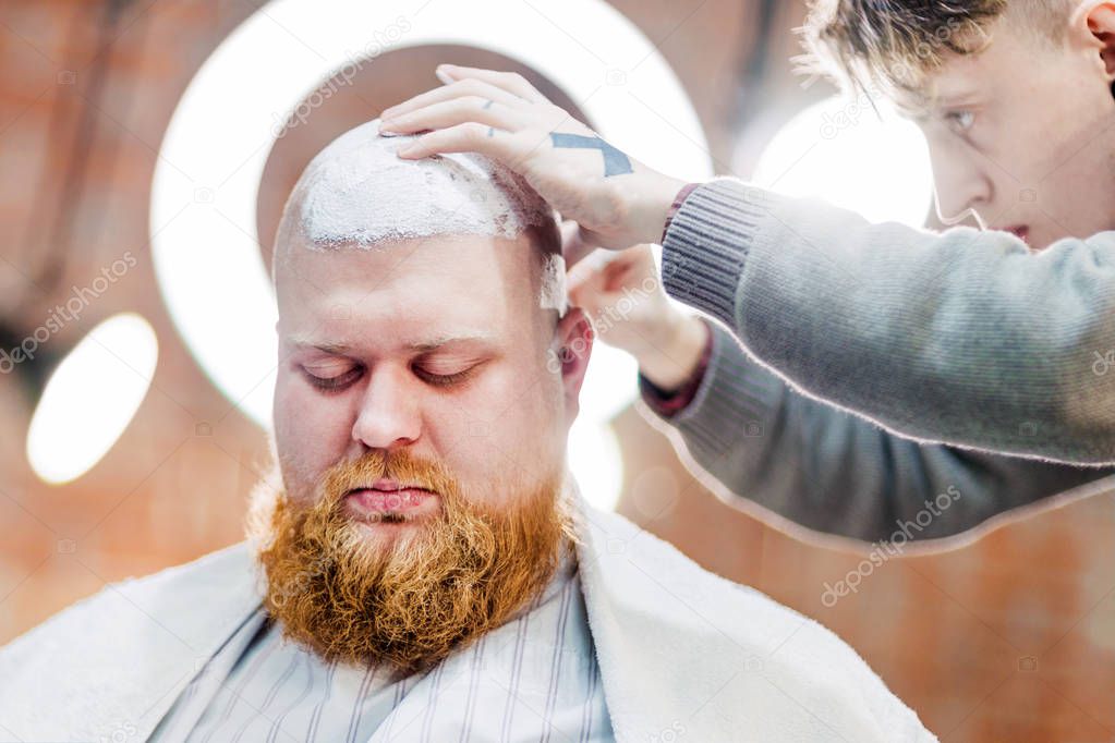 A red bearded man with mustache is sitting in men's beauty salon.