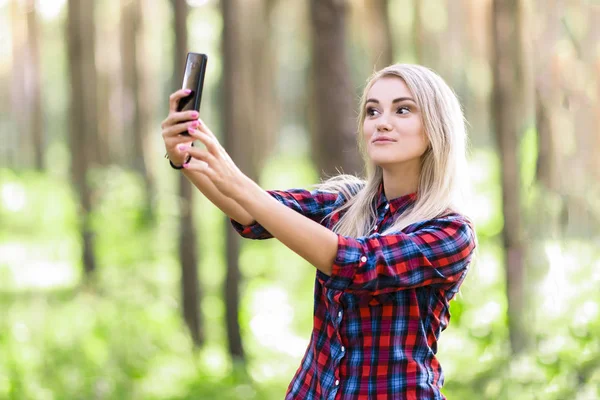 Una ragazza adolescente bionda sta facendo selfie nel parco . — Foto Stock