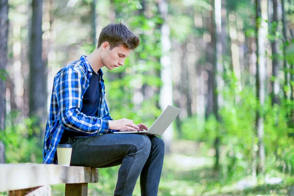 Een jongeman is typen op een laptop in een zomer-forest. — Stockfoto