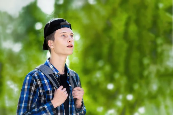 Um jovem com uma mochila está em uma floresta verde . — Fotografia de Stock