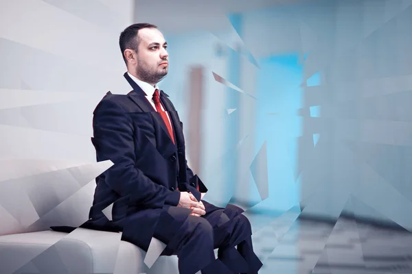 A man in business suit thoughtfully sitting at sofa.