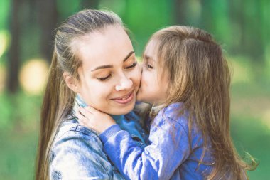 Annem, kollarında kızı öpüyor, hugs. Şefkat, sevgi. Ağaçlar, arka plan üzerinde yakın çekim.