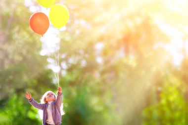 Küçük kız balonlar gökyüzünde bir yeşil orman arka planı sağlar.