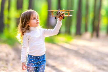 Küçük kız ormanda sarı bir uçak ile oynarken.