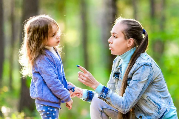 Strict mother talking to her daughter. Walk in the summer forest.