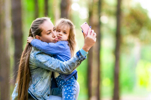 Pozitif anne ve kızı ormanda bir yürüyüşe selfie al. Oynak ruh hali. Yaz güneşli gün.