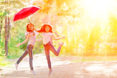 Kırmızı şemsiye yaz ormanda bir yürüyüşe iki oynak kız. Parlak güneşli bir günde.