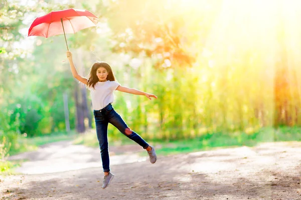 夏の森の散歩に赤い傘ジャンプ十代の少女 明るく晴れた日 — ストック写真