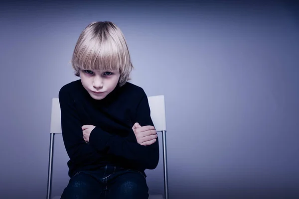 Обиженный блондин маленький мальчик в студии сидит на стуле со своим — стоковое фото