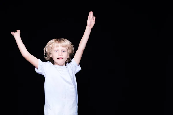 Blond little boy raised his hands up in a white T-shirt on a bla — Stock Photo, Image