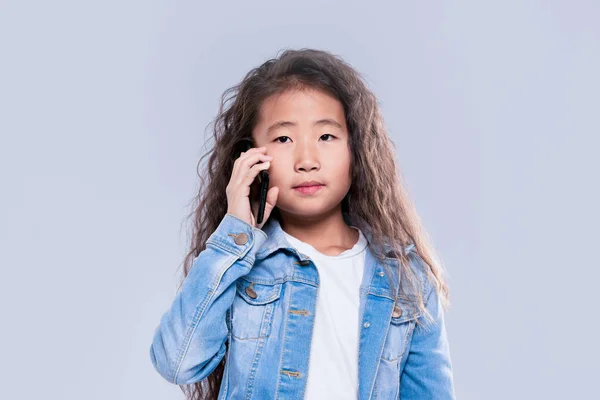 Et jentebarn som snakker i en mobiltelefon. Smarttelefon. På en lys rygg – stockfoto