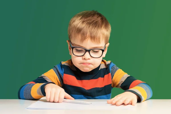 Beleidigter Junge mit Brille sitzt an einem Schreibtisch. Nahaufnahme — Stockfoto