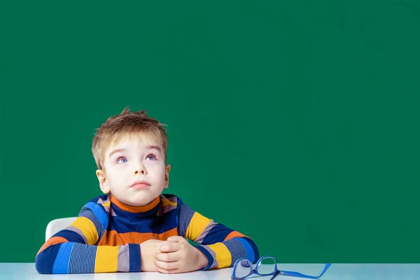 Το αγόρι που ονειρεύεται, κάθεται στο γραφείο του. Πράσινο φόντο. Αντιγραφή χώρου — Φωτογραφία Αρχείου