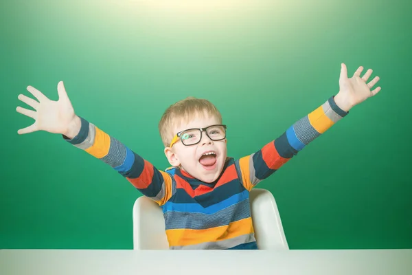 Laughing boy in glasses is sitting at the desk, shouting joyfull — Stock Photo, Image