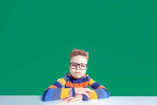 Мальчик в очках, строгий взгляд, сидит за столом. Копирование пространства — стоковое фото
