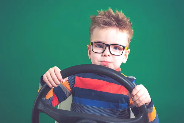 Zabawny chłopak posiada koło kierownicy w jego ręce, na tył zielony — Zdjęcie stockowe