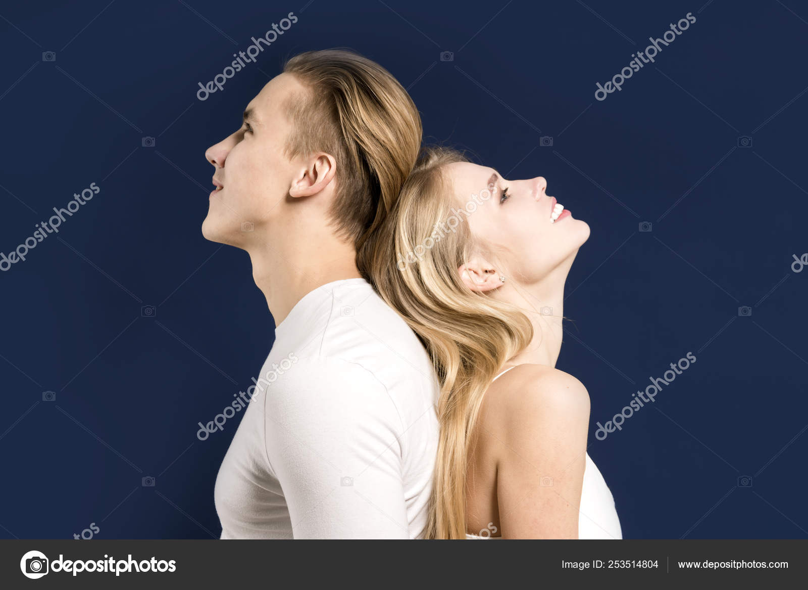 Smiling couple back to back posing in the studio on a dark blue stock