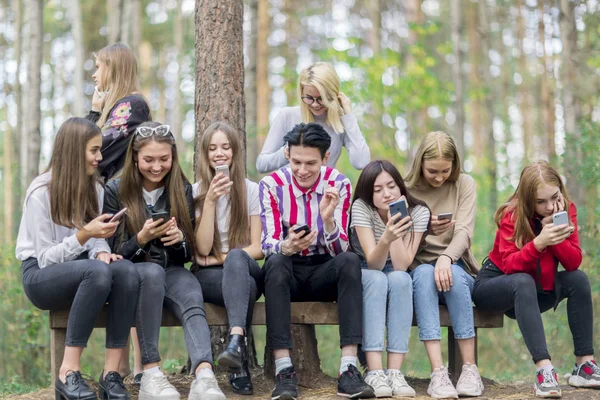 Teenageři s telefony v letním lese sedí na Benc — Stock fotografie