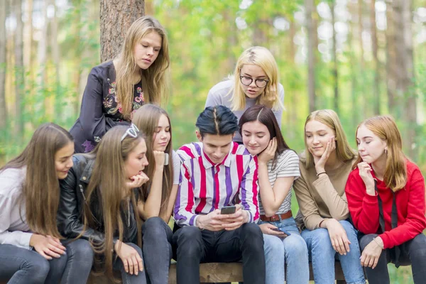 Un groupe d'adolescents regarde au téléphone alors qu'ils sont assis sur un ben — Photo