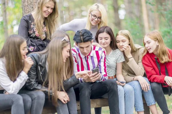 Mladí lidé sedí na lavičce v lese a dívají se na pho — Stock fotografie