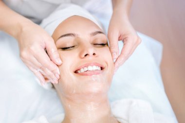 Kozmetoloji. Güzellik maske ile yüz masajı yapar. Spa prosedürü genç güzel kız