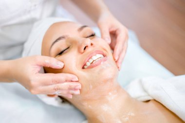 Maske ile yüz masajı yaparken Kozmetolog elleri yakın. Spa prosedürinde gülümseyen kız