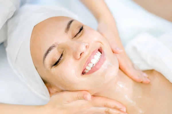 Kozmetoloji. Bir Kozmetolog elleri bir maske ile yüz masajı yapmak. Spa prosedürinde gülümseyen kız