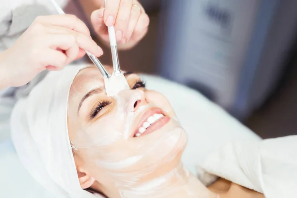 Kozmetoloji. Kozmetolog bir temizlik yüz maskesi uygular. Yüz gençleştirme prosedürü üzerinde gülümseyen kız. Spa yüz prosedürü