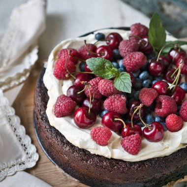 Ahududu, yaban mersini ve nane yaprakları ile rustik arka plan üzerinde mascarpone ile çikolatalı kek.