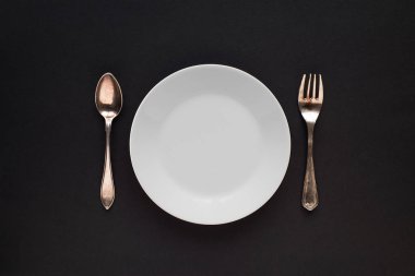 Beyaz tabak, kaşık ve çatalı, siyah bir arka plan